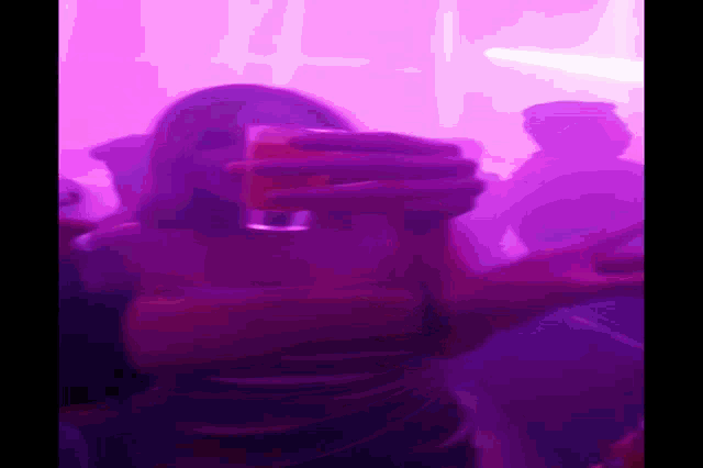 a person is holding a glass in front of a pink light