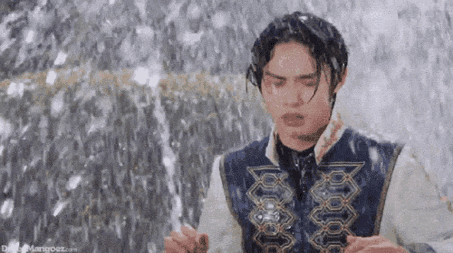 a young man is standing in front of a waterfall .