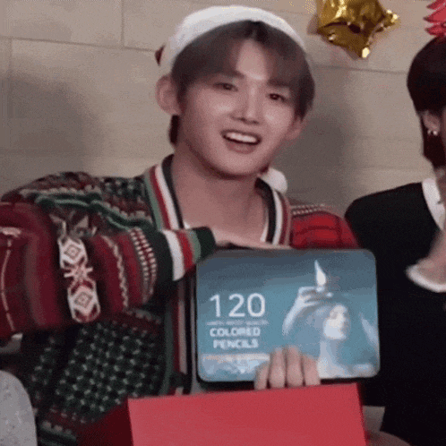 a man in a santa hat is holding a box of 120 colored pencils .