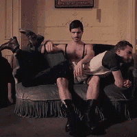 two men are sitting on a couch and one of them is spanking another man