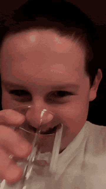 a young boy is drinking from a glass with a straw