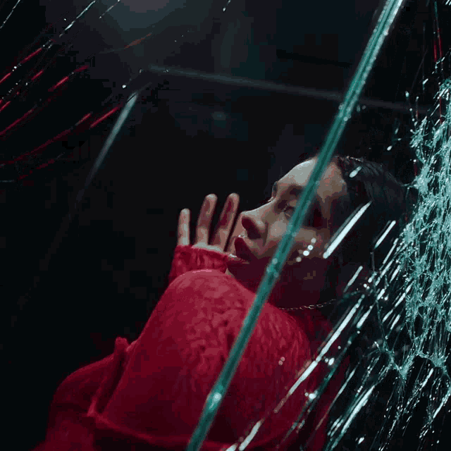 a woman in a red dress looks at her reflection in a broken mirror