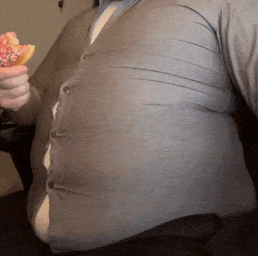 a man in a grey shirt holds a donut with pink sprinkles