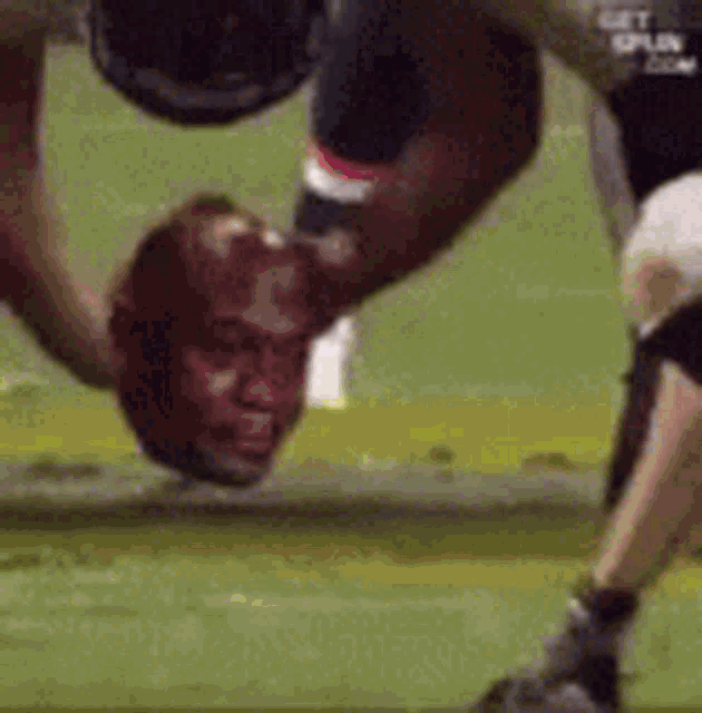 a football player is doing a handstand on a field with his head in the air .