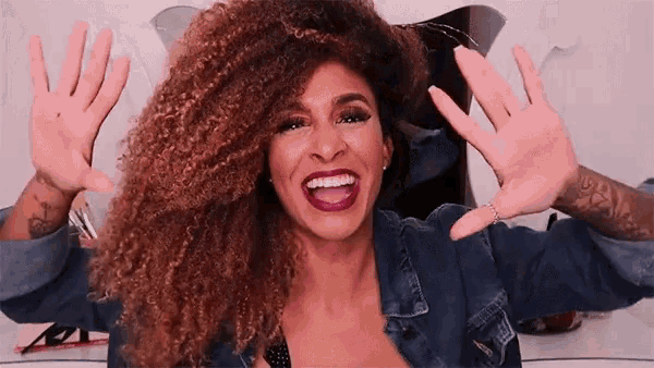 a woman with curly hair is smiling and waving