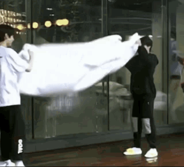 a man is holding a large white cloth in front of a window .