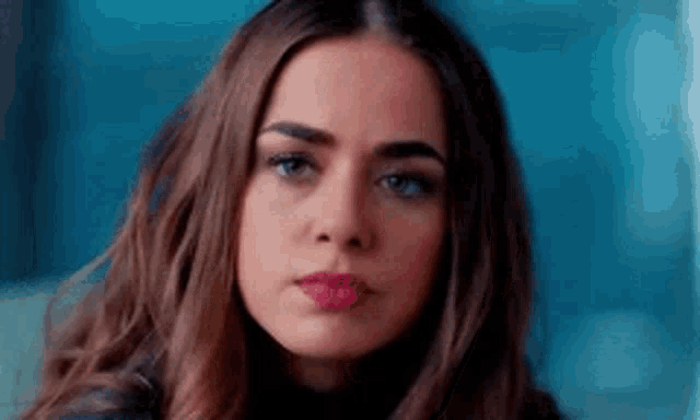 a woman with long hair and red lipstick is looking at the camera with a serious look on her face .