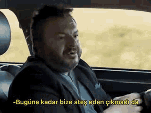 a man in a suit and tie is sitting in the back seat of a car with a caption .