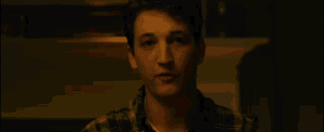 a young man in a plaid shirt is sitting in a dark room .