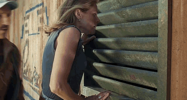 a woman is peeking out of a window while a man stands behind her .