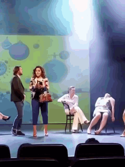 a group of people on a stage including a woman with a purse talking to a man