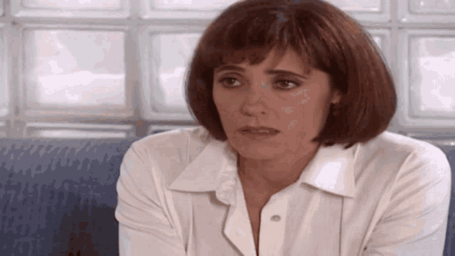 a woman in a white shirt is sitting on a blue couch and looking at the camera