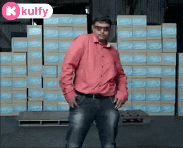 a man in a pink shirt and jeans is dancing in front of a stack of boxes .