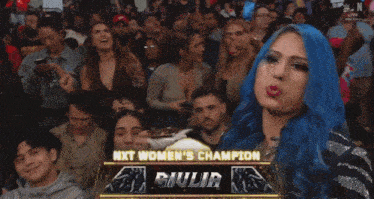a woman with blue hair is holding a trophy in front of a crowd of people