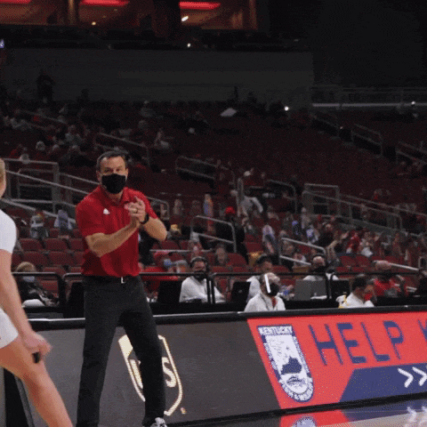 a man wearing a mask stands in front of a kentucky basketball sign
