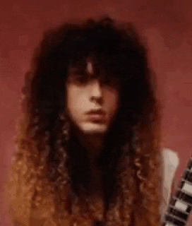 a man with long curly hair is holding a guitar and making a funny face .