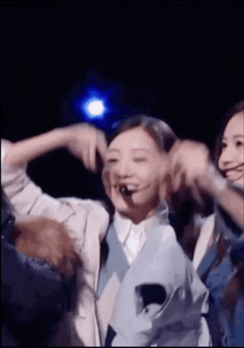 a group of women are dancing on a stage and one of them has a microphone in her mouth .