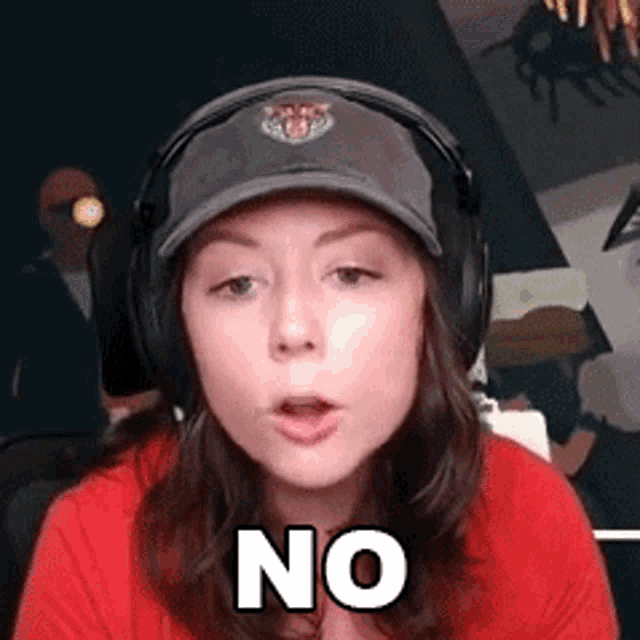 a woman wearing headphones and a baseball cap is making a no sign .