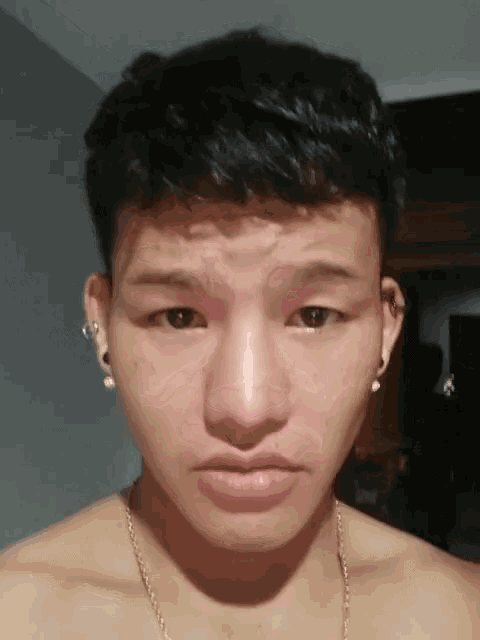 a young man without a shirt is wearing earrings and a necklace