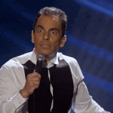 a man in a white shirt and black vest holds a microphone