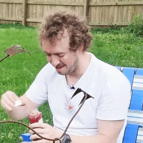 a man with curly hair is sitting on a blue and white chair in the grass