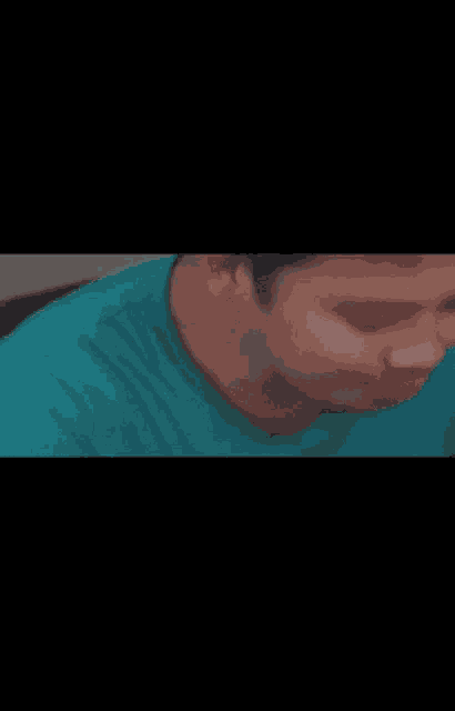 a man in a blue shirt is sitting at a table with a fork in his mouth