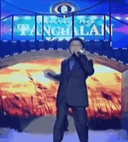 a man in a suit is singing into a microphone on a stage in front of a sign that says tanghalang