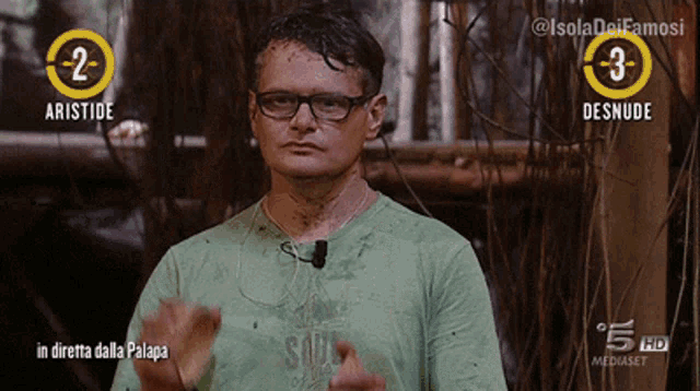 a man wearing glasses and a green shirt stands in front of a sign that says aristode on it
