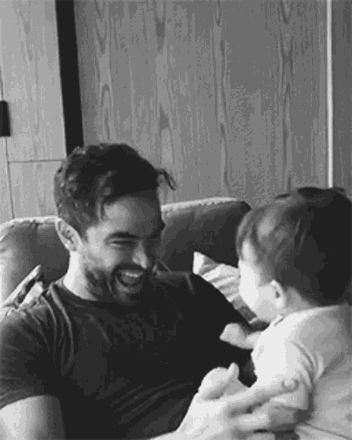 a man is sitting on a couch holding a baby in his arms .