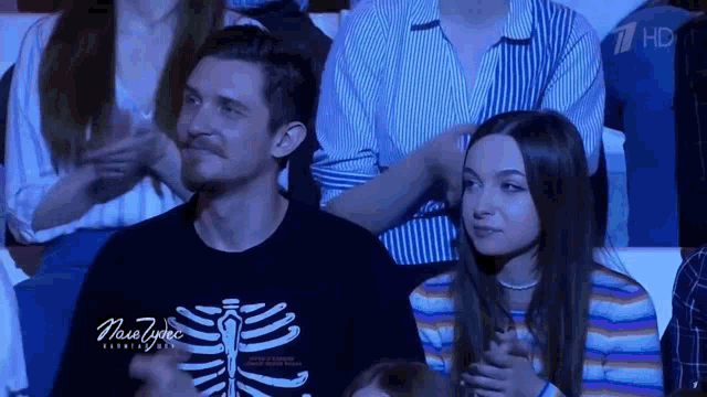 a man wearing a shirt with a skeleton on it sits next to a woman in a striped shirt