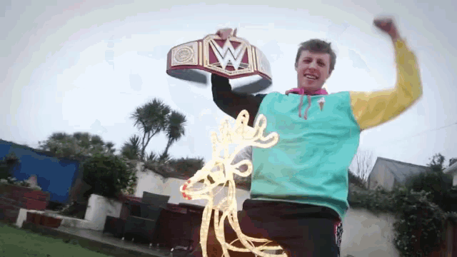 a man in a blue and yellow sweatshirt holds up a wrestling belt with the letter w on it