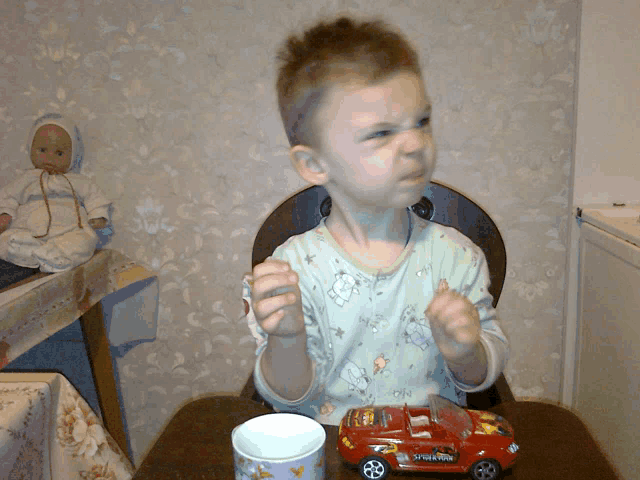 a little boy sitting at a table with a toy car that says spiderman