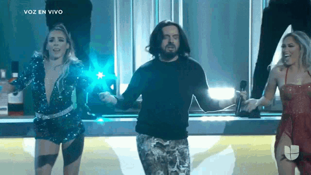 a man and two women are dancing on a stage with the words voz en vivo in the upper right corner