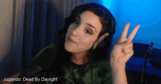 a woman wearing headphones gives a peace sign in front of a microphone