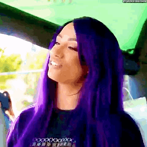 a woman with long purple hair is smiling in a car .