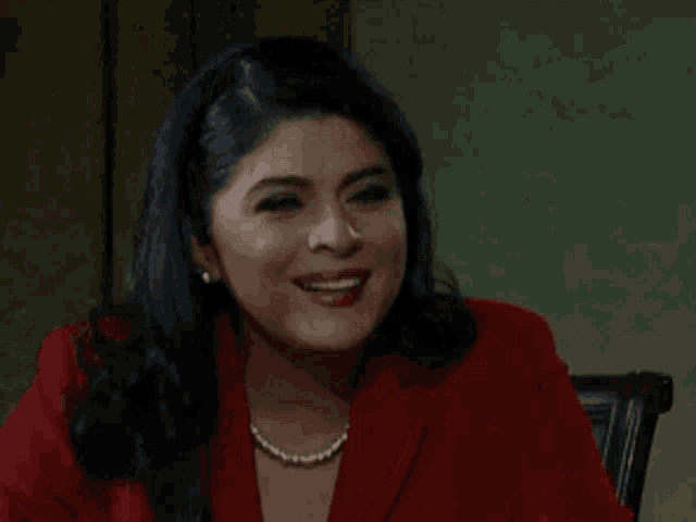 a woman in a red jacket and pearl necklace is smiling while sitting at a table .