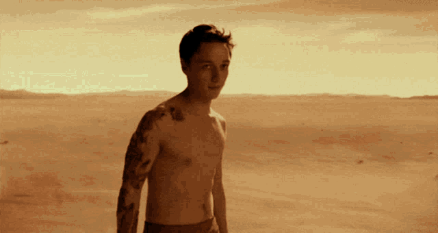 a shirtless man with a tattoo on his arm stands in a desert