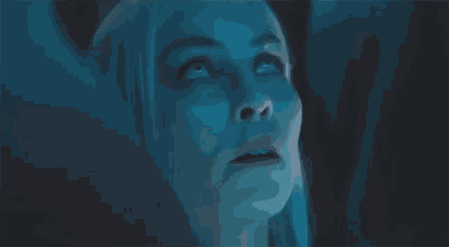 a close up of a woman 's face in a dark room looking up at something .