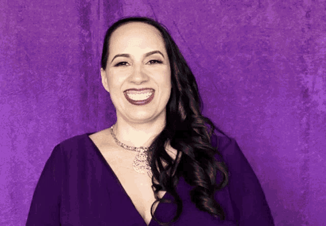 a woman wearing a purple top and a necklace is smiling