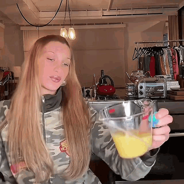 a woman in a camo jacket is holding a measuring cup of liquid .