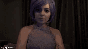 a woman with purple hair is wearing a gray sweater and looking at the camera .