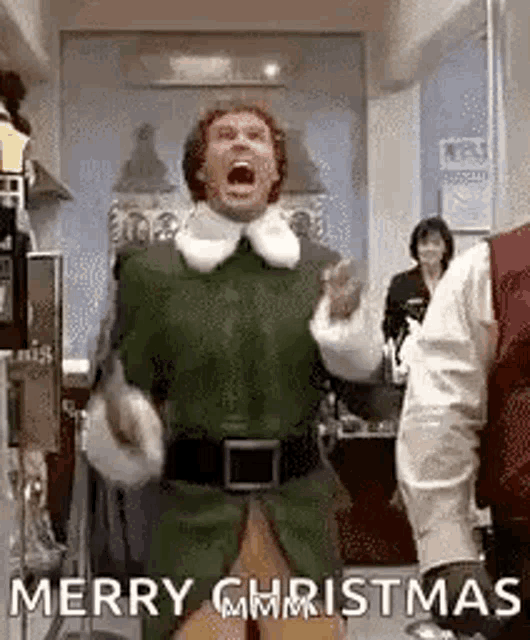 a man in a green elf costume is standing in a room with his mouth open .