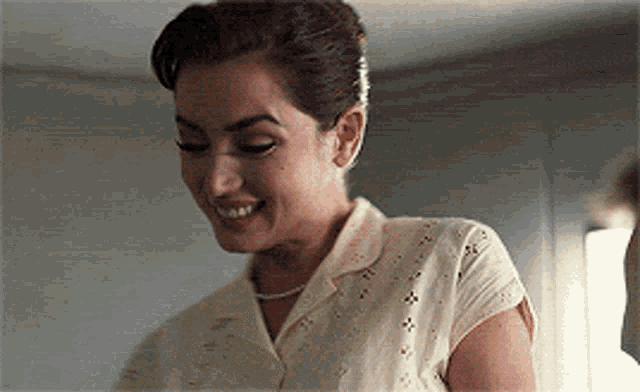 a woman in a white shirt is smiling and looking down