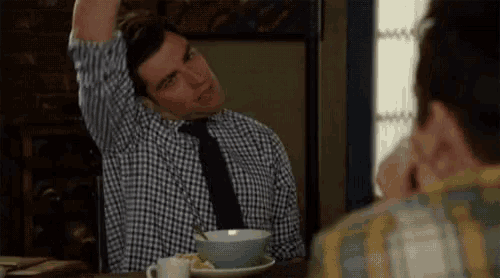 a man in a plaid shirt and tie is stretching his arm while sitting at a table with a bowl of food .