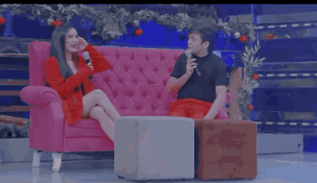a man and a woman are sitting on a pink couch and talking into microphones