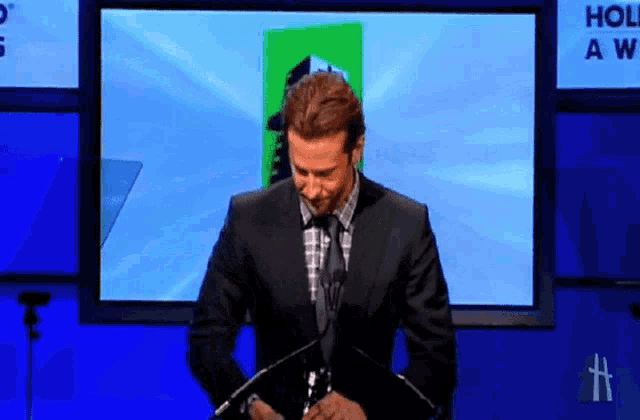 a man in a suit and tie is standing in front of a screen that says hollywood awards