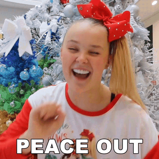a girl with a red bow in her hair is laughing in front of a christmas tree with the words peace out below her