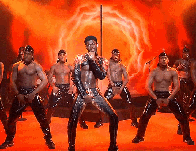 a man is singing into a microphone while a group of men are dancing around him