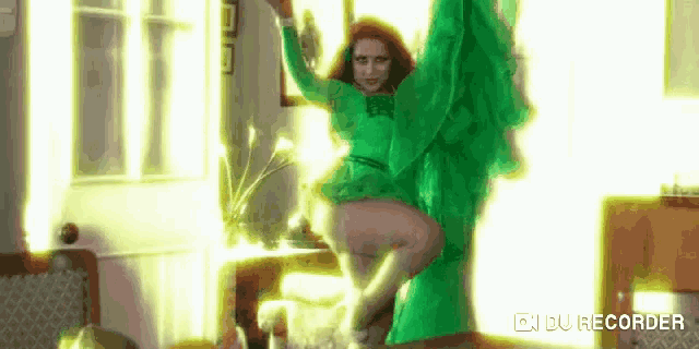 a woman in a green dress is dancing in a living room with her arms outstretched .