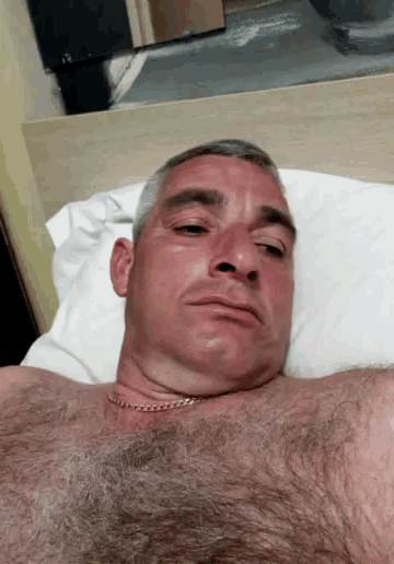 a man laying on a bed with his shirt off and a chain around his neck